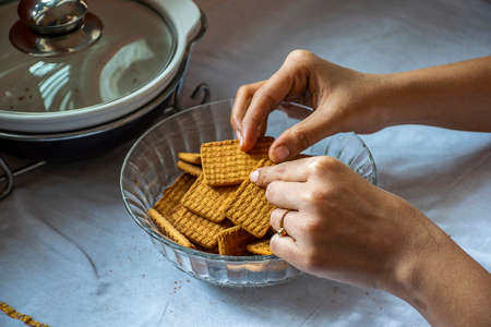 Stock photo of a women taking wheat biscuit from a bowl of biscuits , kept on table on white background. focus on biscuit.の写真素材