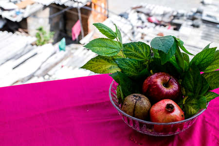 Stock photo of an apple, pomegranate and sapodilla fruit kept in a glass bowl on pink background...