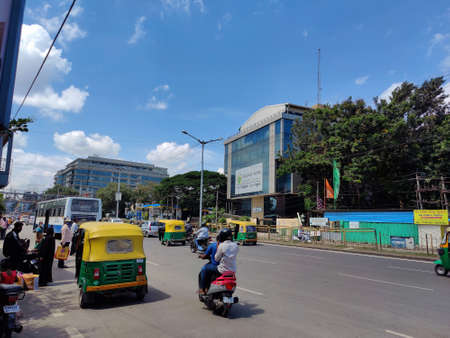 Bangalore, India_ September 21st 2021; Stock photo of people riding vehicles on crawdad road, waiting for bus in bright afterrnoon multistorey corporate buildings surrounding main road in Bangalore.のeditorial素材