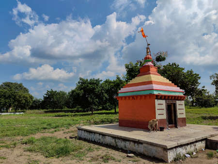 Stock photo small old hindu temple painted with orange color, situated in the middle of grass land, surrounded by green trees, blue sky with white clouds on background. Picture captured at Gulbarga.の写真素材