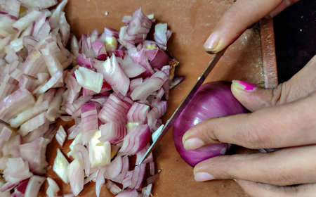 Stock photo of a girl cutting or chopping pink onion on brown color chopping board in the kitchen...