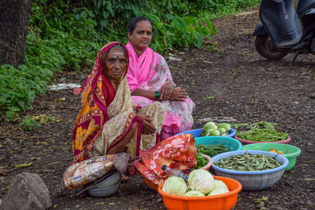Kolhapur,India- September 13th 2019; Stock photo of 40 to 70 age group two Indian women wearing saree and sitting by the roadside, selling farm fresh green vegetables in the monsoon season in India.のeditorial素材