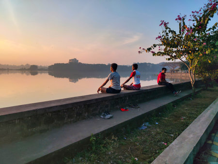 Kolhapur,India- December 5th 2020; Stock photo teenager boys practicing pranayama or yoga or meditation by the lake sitting in lotus pose at Rankala lake. calm and beautiful early morning view.のeditorial素材