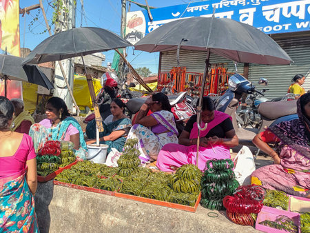 Tuljapur,India- October 28th 2022; Stock photo of Indian women wearing saree sitting on the street and selling traditional green color glass bangles in the crowded market area.hardworking India women.のeditorial素材