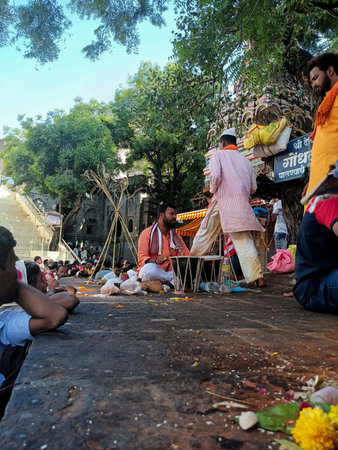Tuljapur, India- october 28th 2022;A middle-aged Indian priest, adorned in traditional attire, plays a folk membranophone instrument during temple ritual,crowd of devoted followers forms the backdrop.のeditorial素材