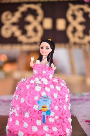 A delightful doll cake, adorned in vibrant pink and embellished with delicate silver balls and white flowers, makes a perfect centerpiece for a little girl's birthday.featuring a detailed doll figure,の写真素材