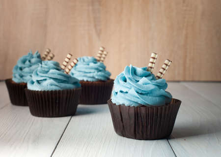 Four cupcakes with blue cream in brown paper form with two wafer tubules on a light backgroundの写真素材