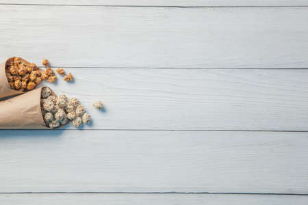 Dragee peanuts in sesame and in sugar in a paper package on a light wooden background