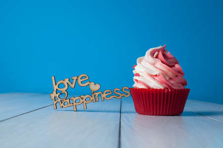 Cupcake with red and white cream in red paper form with love and happiness on a light backgroundの写真素材