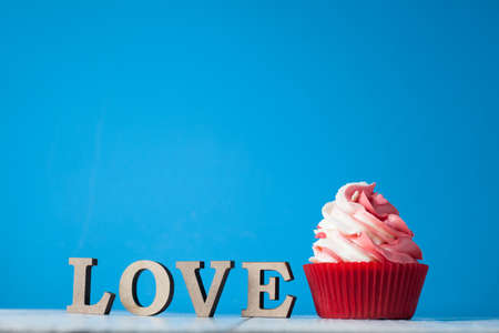 Cupcake with red and white cream in red paper form with wooden letters with the word love on a light backgroundの写真素材