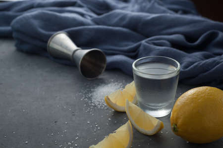 Tequila cocktail with lemons in a glass and salt on a gray background next to a jiger and a gray clothの写真素材