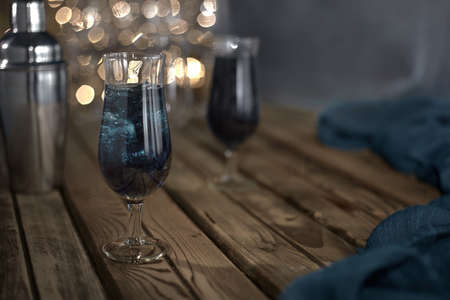 Cocktail with ice blue on a wooden table next to a shaker in the background bokehの写真素材