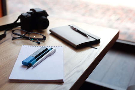 Camera, coffee, diary and pens on a wooden table in the coffee shop in front of the windowの写真素材