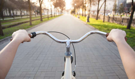 Girl's hands on the wheel of a beige bicycle on the alley in the springの写真素材