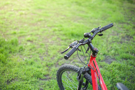 Mountain bike of red color with a black rudder on green grass