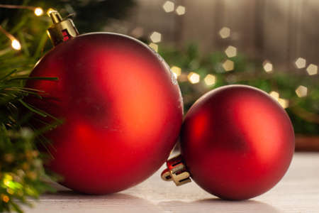 Christmas toy red Christmas balls on a light table top next to a Christmas tree on a background of a garland on a wooden wallの写真素材