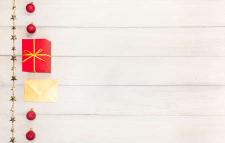 Christmas present in a red box with a gold ribbon and golden envelope next to red Christmas balls on...