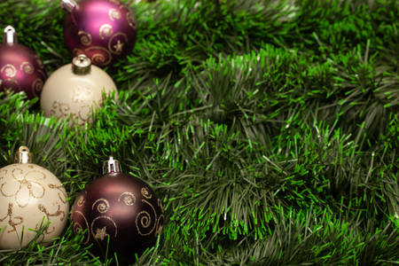 Christmas toy white ball and purple ball with patterns on green tinsel on a wooden backgroundの写真素材