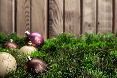 Christmas toy white ball and purple ball with patterns on green tinsel on a wooden backgroundの写真素材