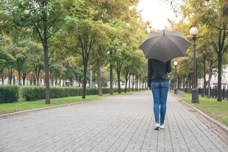 girl in a black leather jacket and blue jeans with a black umbrella in her hands on the mallの写真素材