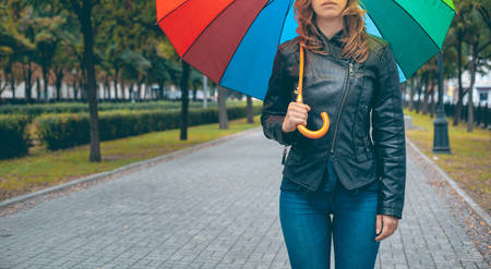girl in a black leather jacket and blue jeans with a multi-colored umbrella in her hands on the mallの写真素材