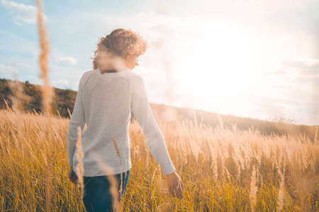 Girl in a white sweater and jeans in a field with spikelets against the blue sky in the rays of the sunの写真素材
