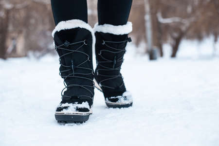 Black winter women's boots with white fur and white soles on the snow in the parkの写真素材