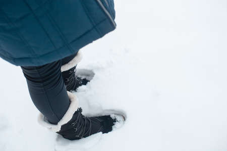 Black winter women's boots with white fur and white soles on the snow in the parkの写真素材