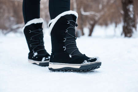 Black winter women's boots with white fur and white soles on the snow in the parkの写真素材