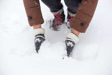 Girl in a brown jacket and gray winter gloves with fur picks up snowの写真素材