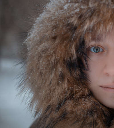 The face of a girl in a hood with fur powdered with snow close-upの写真素材