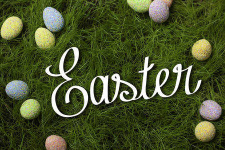 Easter eggs of different colors on the lawn in the green grass are around the inscription Easter