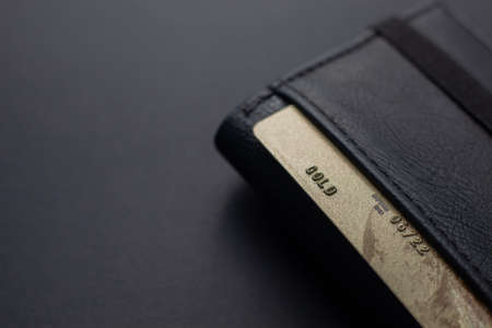 Black leather wallet with a gold credit card on an isolated black backgroundの写真素材