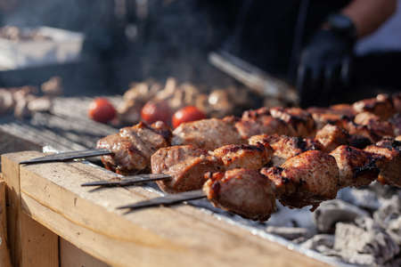 Skewered meat is cooked on hot coals by a cook in black uniform and gloves.の写真素材