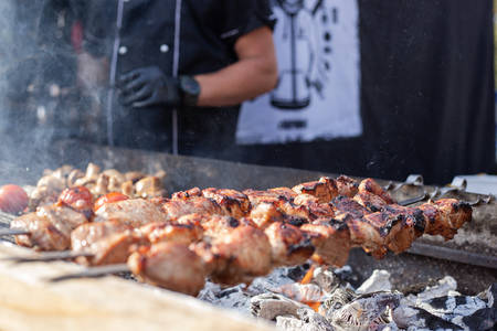 Skewered meat is cooked on hot coals by a cook in black uniform and gloves.の写真素材