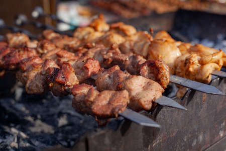 Meat on a skewer is fried on hot charcoal on an iron barbecue.の写真素材