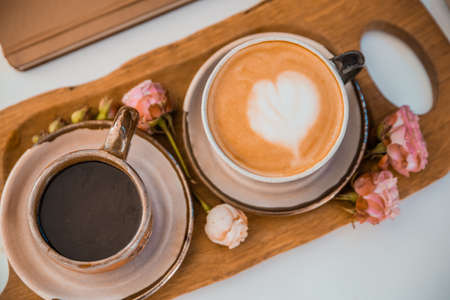 Two cups of coffee decorated with hearts on a wooden tray decorated with roses are on a white table