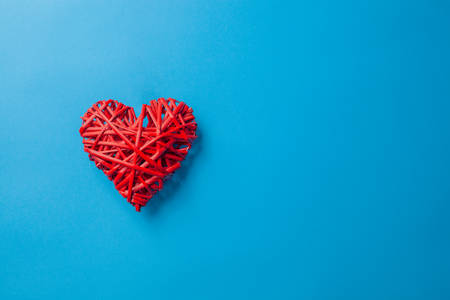 Red wicker heart made of twigs on a blue background with place for text