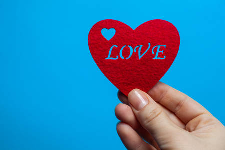 Decorative heart of red color with the inscription love in the hands of a man on a blue backgroundの写真素材