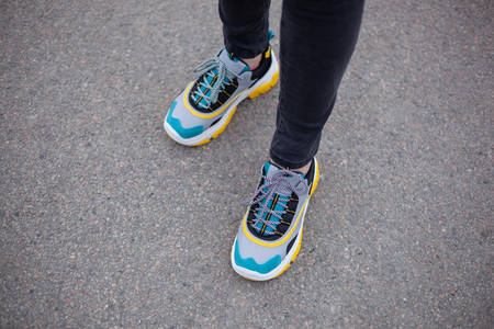 Feet shod in sneakers multi-colored yellow, white, black and blue are on the asphalt road. Close-upの写真素材