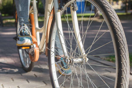 Feet shod in bright sneakers stand on the pedals of a beige bicycle