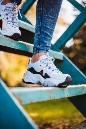 White sneakers with black inserts on female legs dressed in jeans on the iron stairs in the park