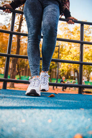 Legs of a girl in jeans and white sneakers with black inserts who stands next to an iron fenceの写真素材