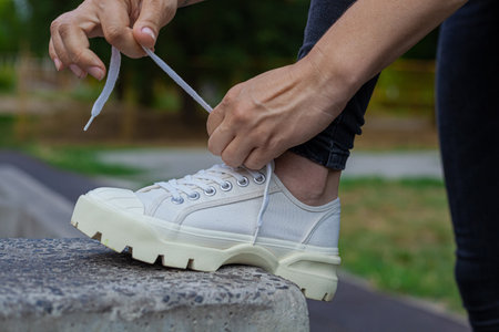 Girl in white sneakers and black jeans tying her shoelacesの写真素材