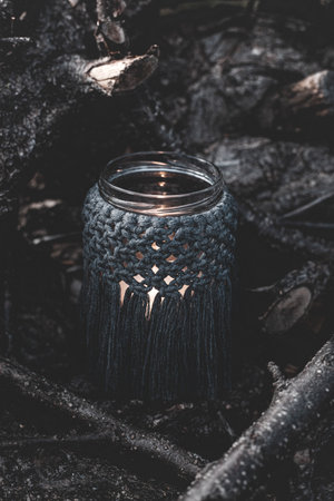Jar with a burning candle decorated with knitted macrame fabric