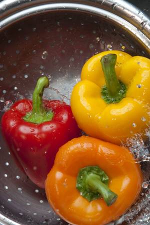 Yellow, red, and orange bell peppers washed in stainless steel metal collinderの写真素材
