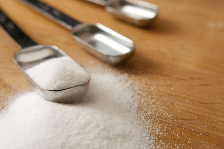 Measurings Spoons on Wood Counter with Sugar. Focus on edge of tablespoon (left most) and sugar granules.. Focus on front edge of tablespponの写真素材