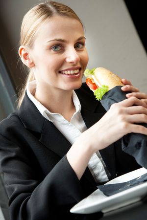 young smiling businesswoman eating a sandwich and looking at cameraの写真素材