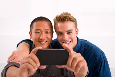Two smiling young men taking self portrait with cell phoneの写真素材