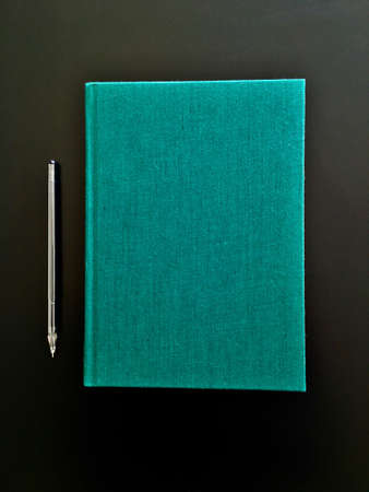 view of closed green cover notebook with pencil on black desk backgroundの写真素材